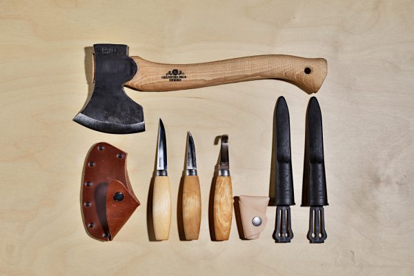 A flay lay of Swedish wood carvign tools that are in the Complete Carving Kit. A Gransfors Bruk Large Carving Axe lays acorss the top of the image with two straight knives and a hookknife from Morakniv
