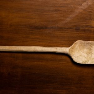 a hand-carved spoon wood is blonde on darker wood background