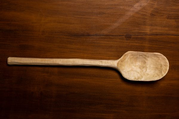 a hand-carved spoon wood is blonde on darker wood background